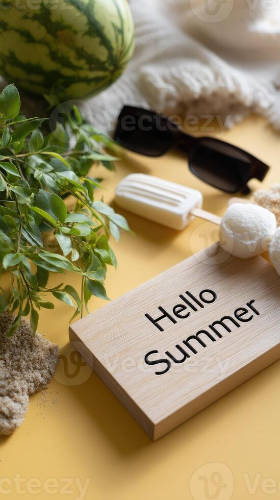 Hello summer sign on a wooden plate with a watermelon, sunglasses, and a beach towel photo