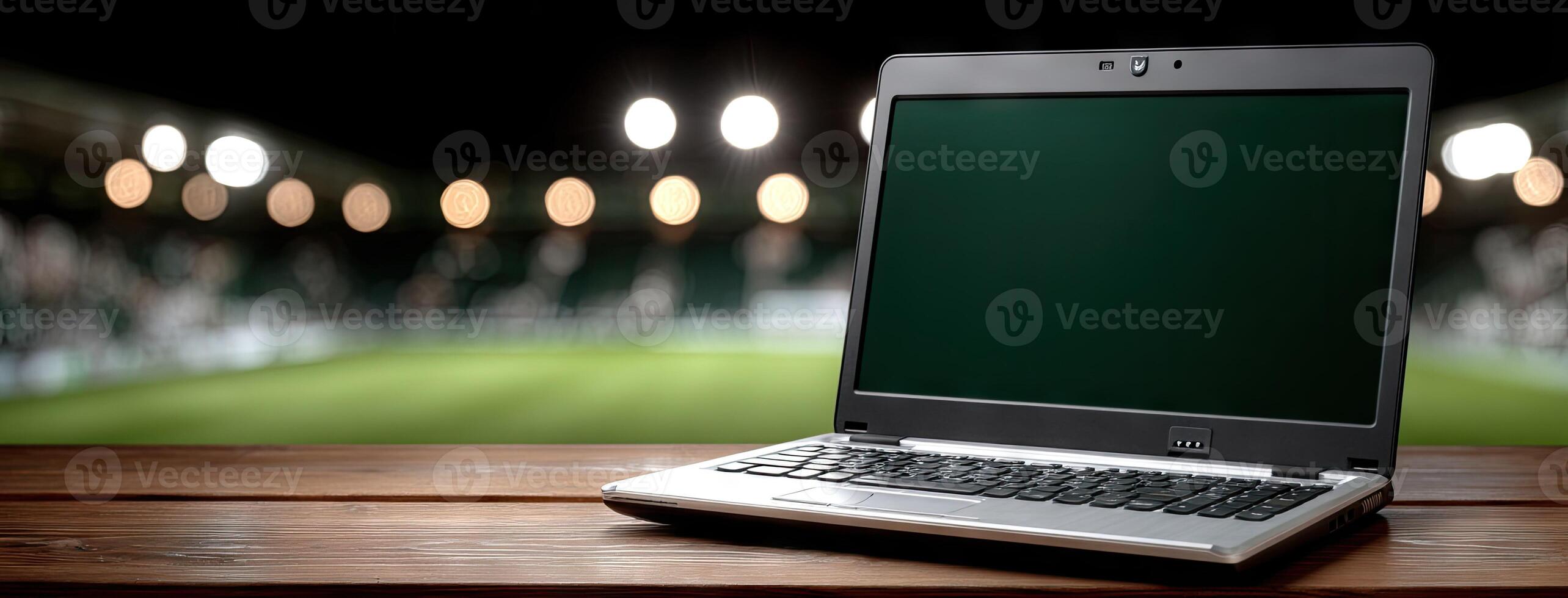 A laptop computer sitting on a wooden table in front of a soccer field photo