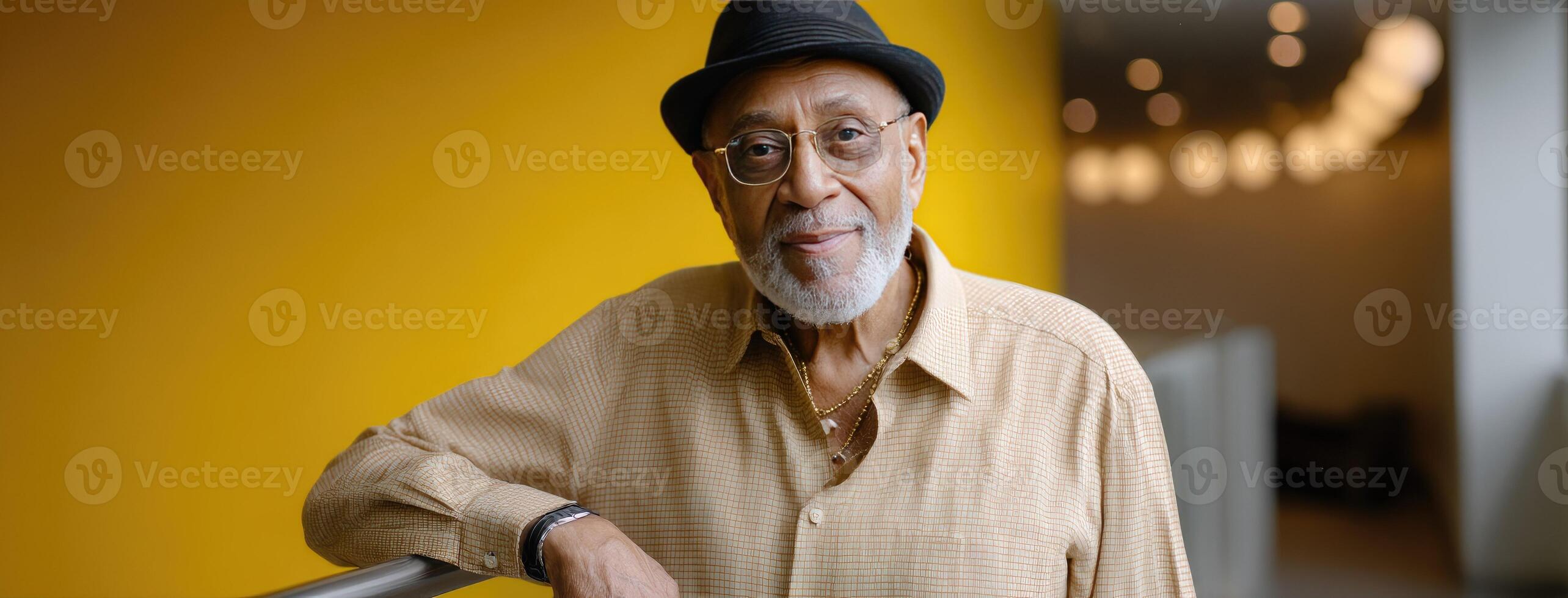 A man with a hat and glasses standing in front of a yellow wall photo