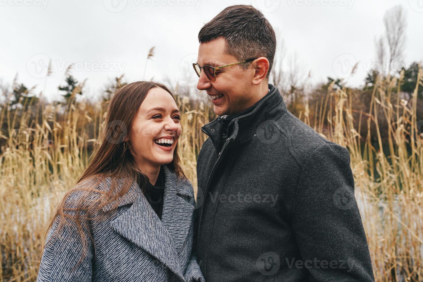 Couple enjoying a joyful moment by a serene lake surrounded by tall grass on a cloudy day in early spring photo