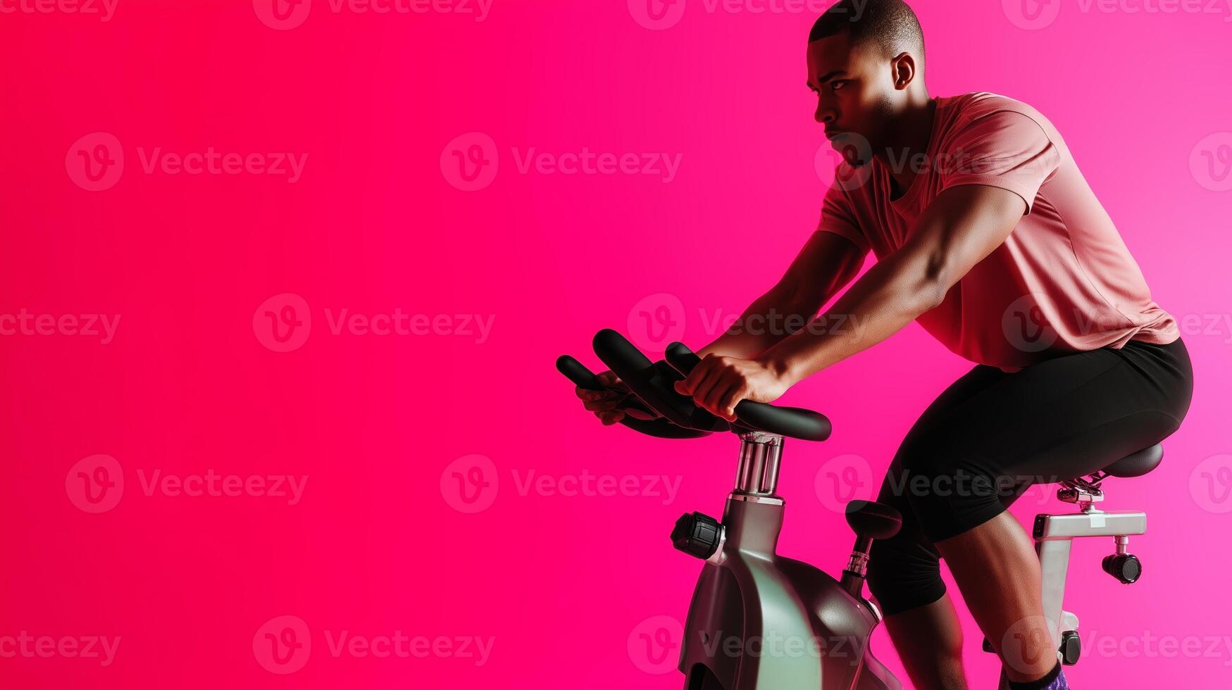 Man exercising on stationary bike against a bright pink background during indoor workout session photo