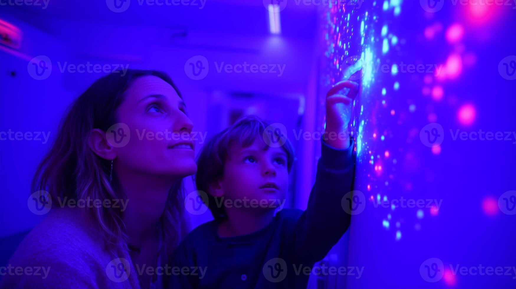 Mother and child exploring colorful light patterns in an interactive space during an evening visit photo