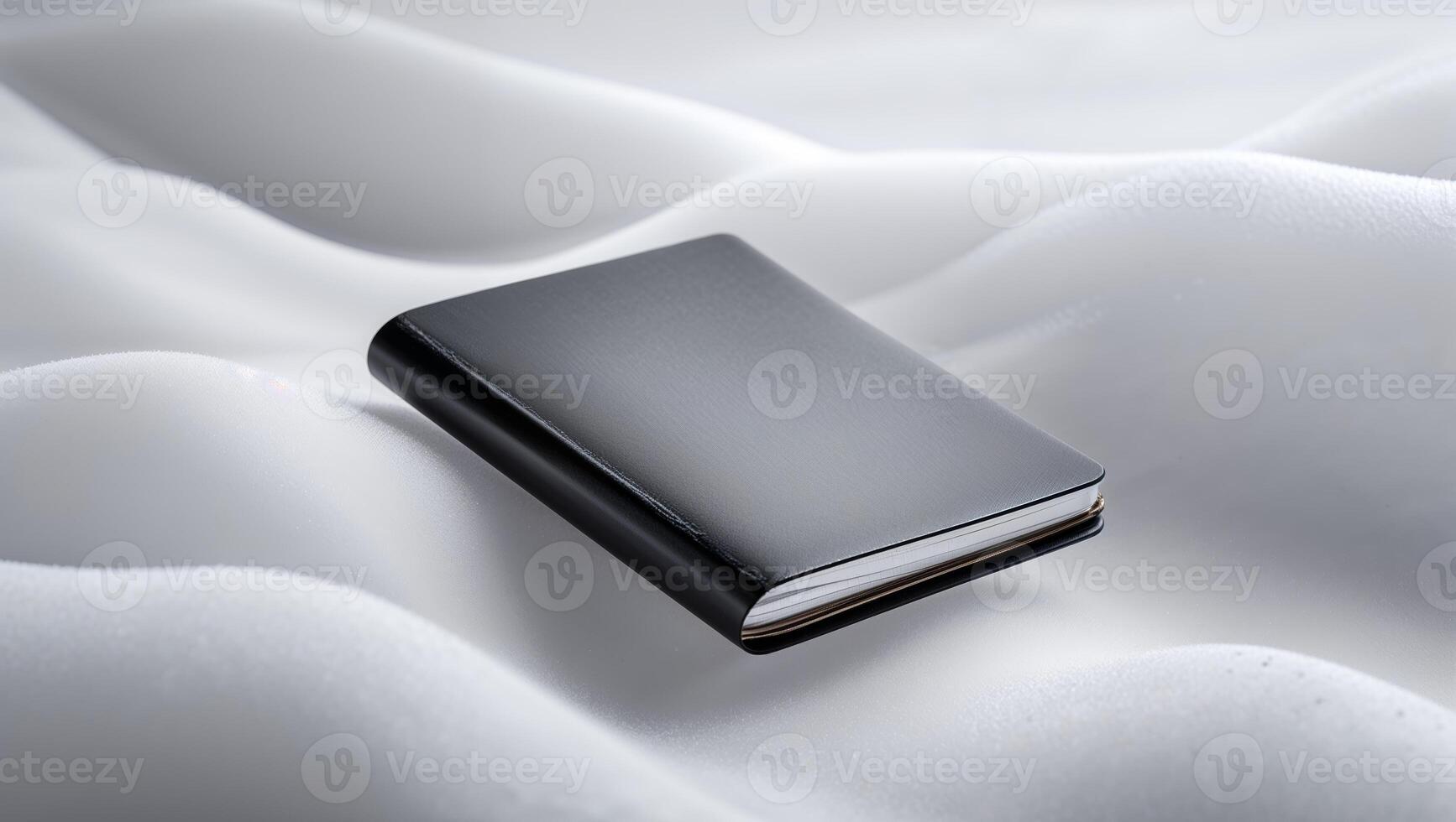 Black notebook resting on a soft, white surface with gentle curves in a tranquil setting photo