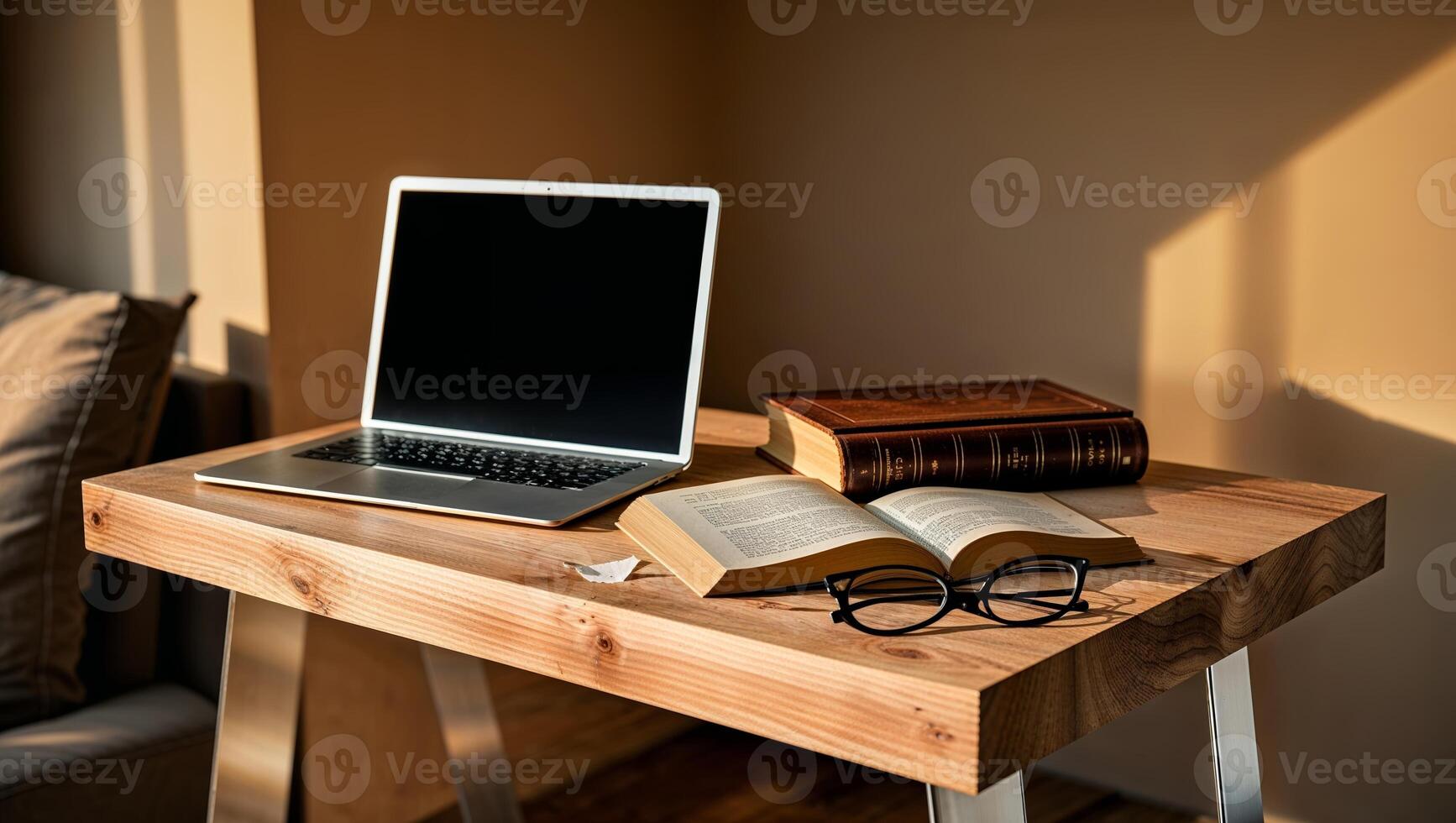 Cozy workspace with a laptop, books, and glasses in a warmly lit room during late afternoon photo