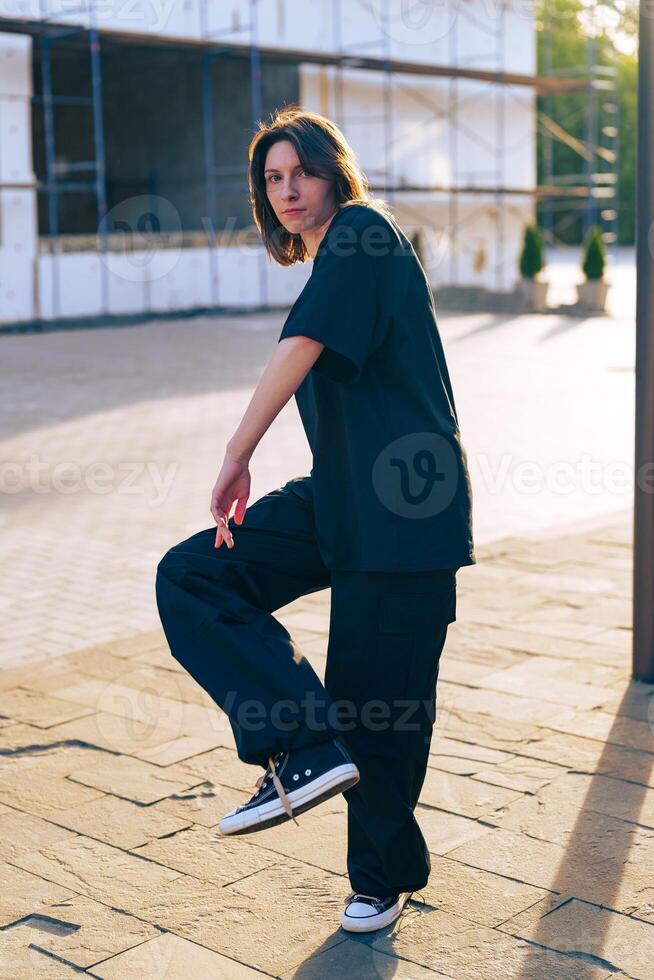 Person striking a pose in casual outfit on a sunny day at a construction site in an urban area photo