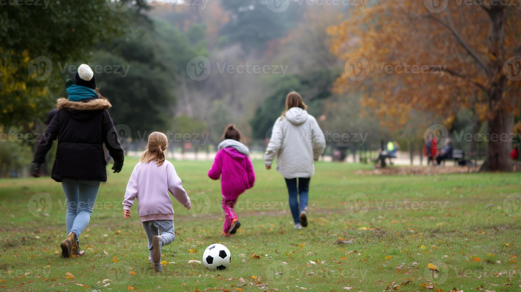 Children playing soccer together in a park during a cool autumn day while leaves fall from the trees photo
