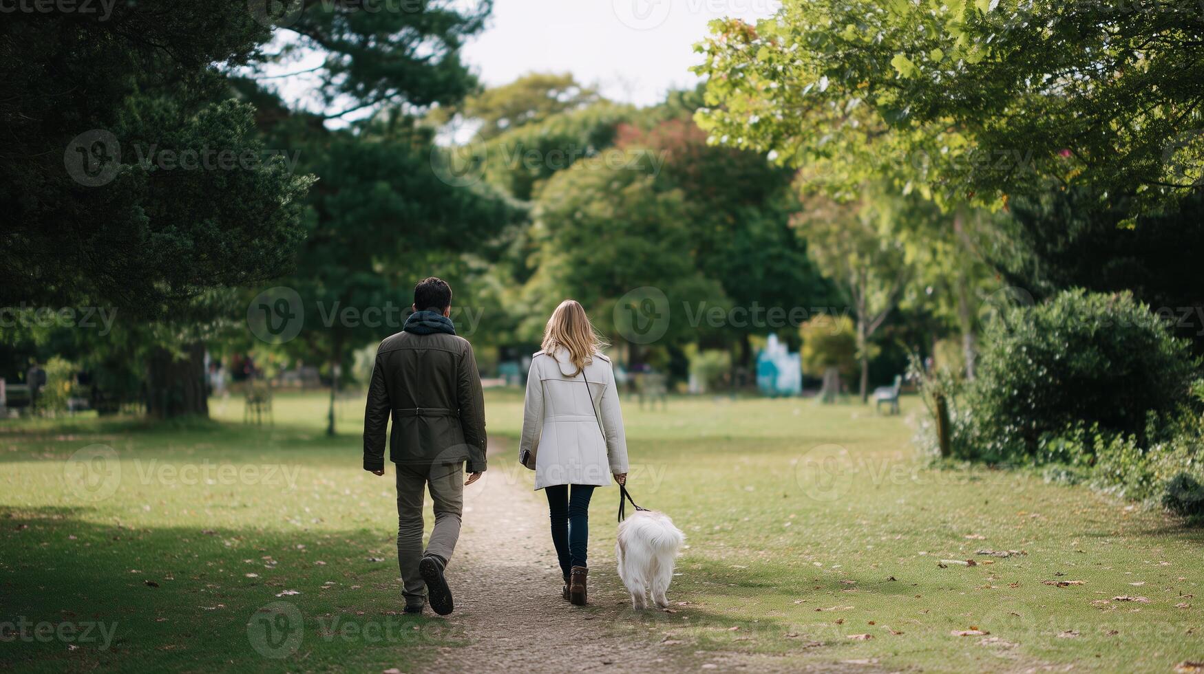Couple enjoys a leisurely walk with their dog on a sunny day in the park surrounded by lush greenery photo