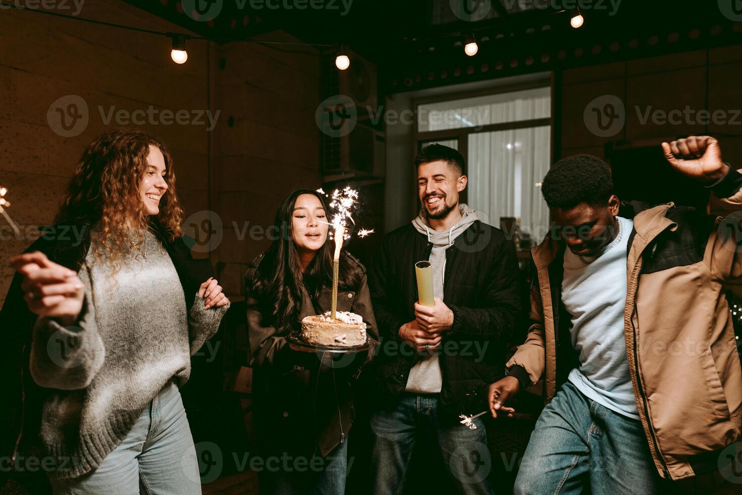 Group of friends celebrating a birthday with cake and sparklers in a cozy outdoor setting at night photo