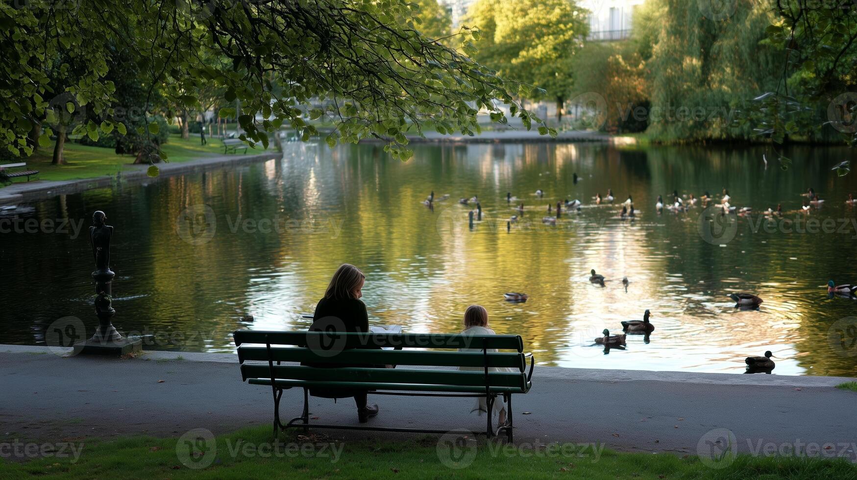 Two people sit on a bench by a tranquil lake surrounded by lush greenery and ducks during late afternoon sunlight photo