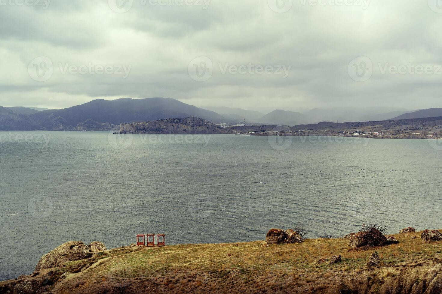 Cloudy sky over a tranquil lake with distant mountains and rocky shoreline photo