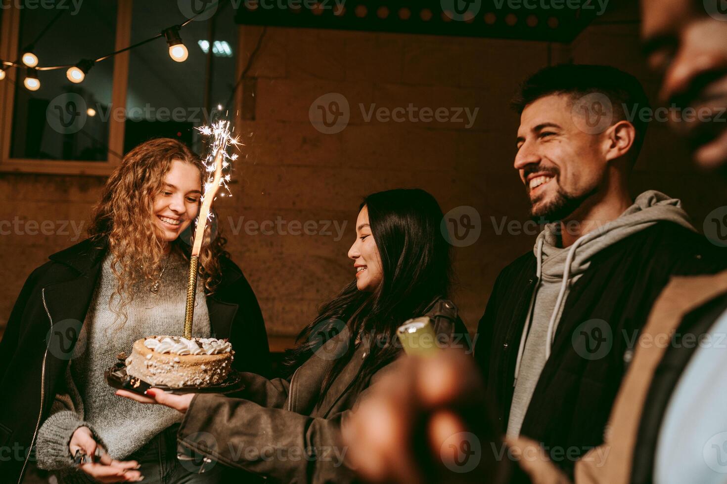 Friends celebrate together at a lively birthday gathering featuring a cake with a sparkler at night photo