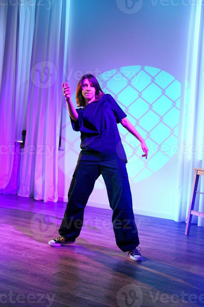 Dancer performing solo in a dimly lit studio with vibrant lighting during a contemporary dance session photo