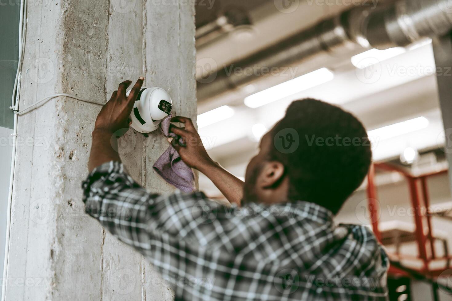 Worker cleans surveillance camera in an industrial setting during daylight hours photo