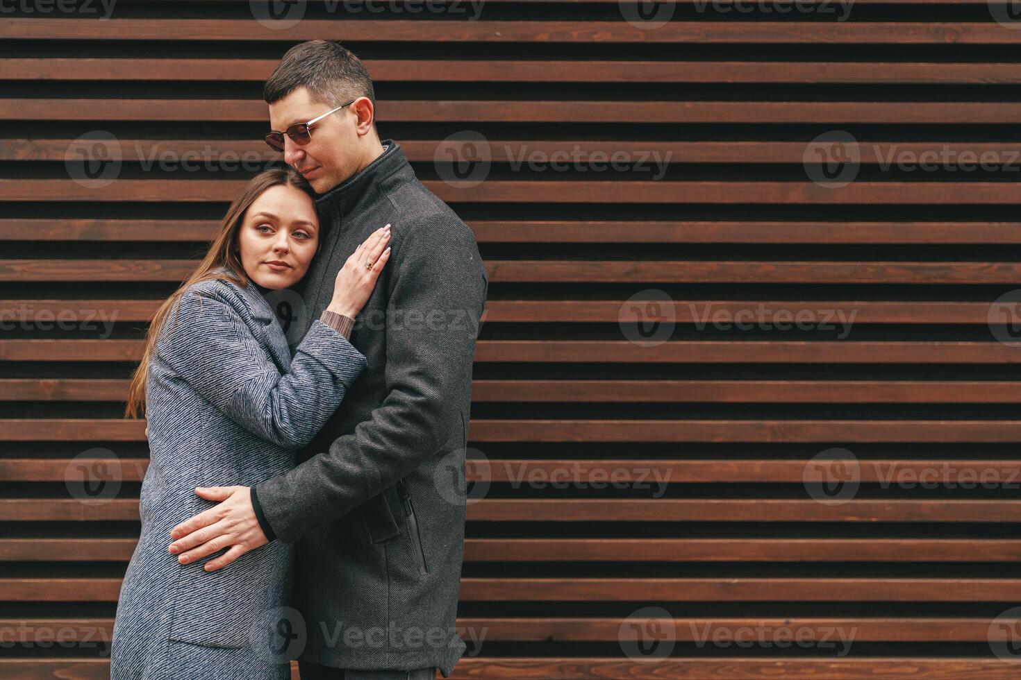 Couple embraces against wooden wall in urban setting, capturing a moment of intimacy and connection during a cool day photo