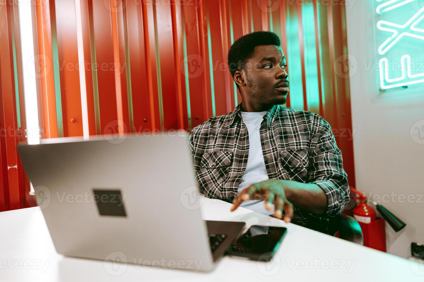 Young man working on laptop in modern workspace with vibrant red walls and neon lights photo