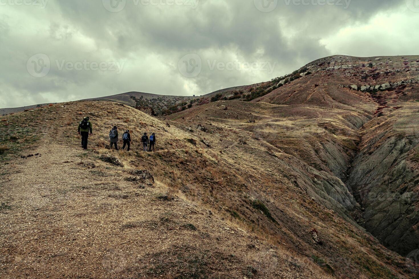 Hikers traverse rugged terrain under cloudy skies in a remote landscape during late afternoon photo