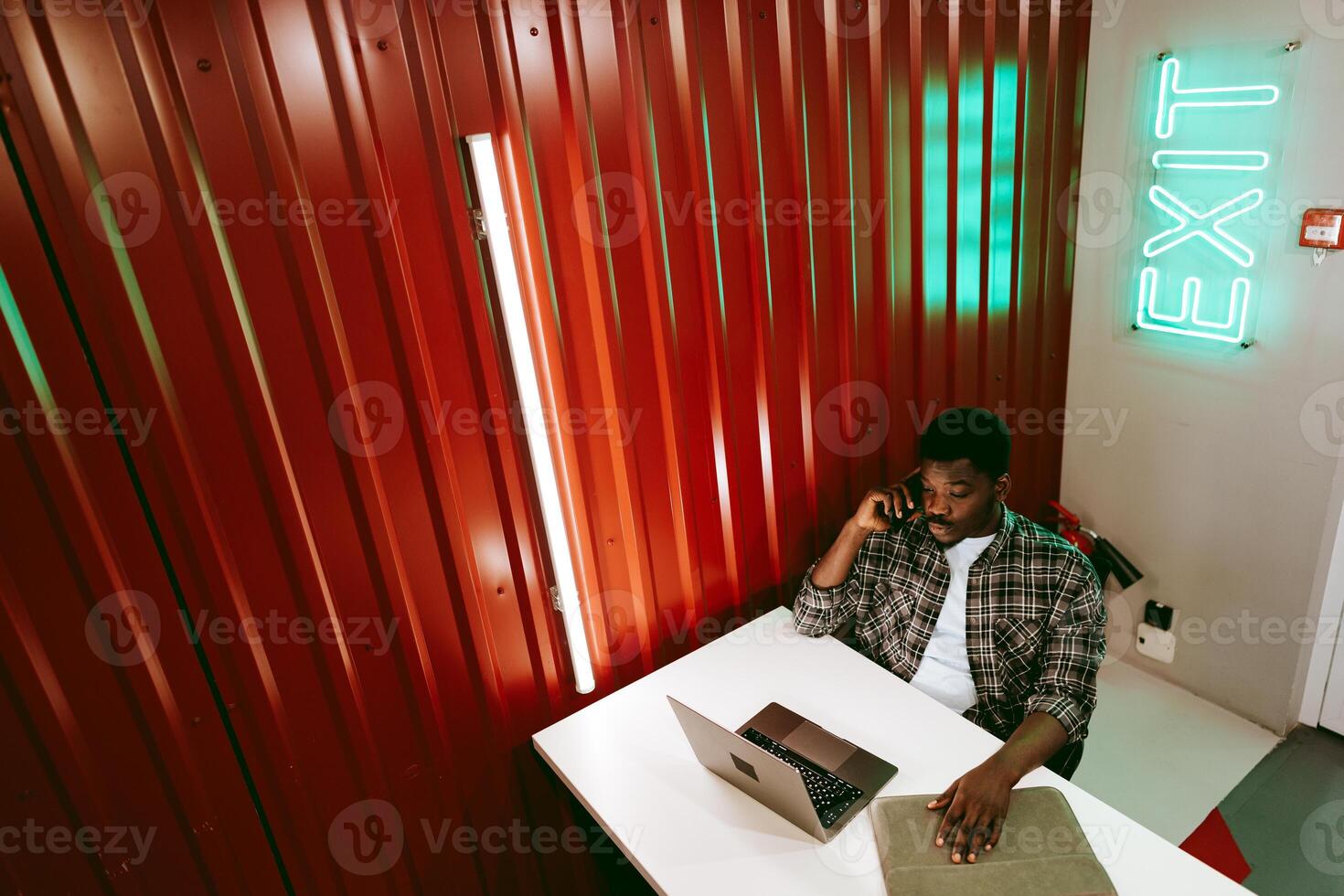 Working professional engaged in a phone call while using a laptop in a modern workspace with distinct wall colors photo