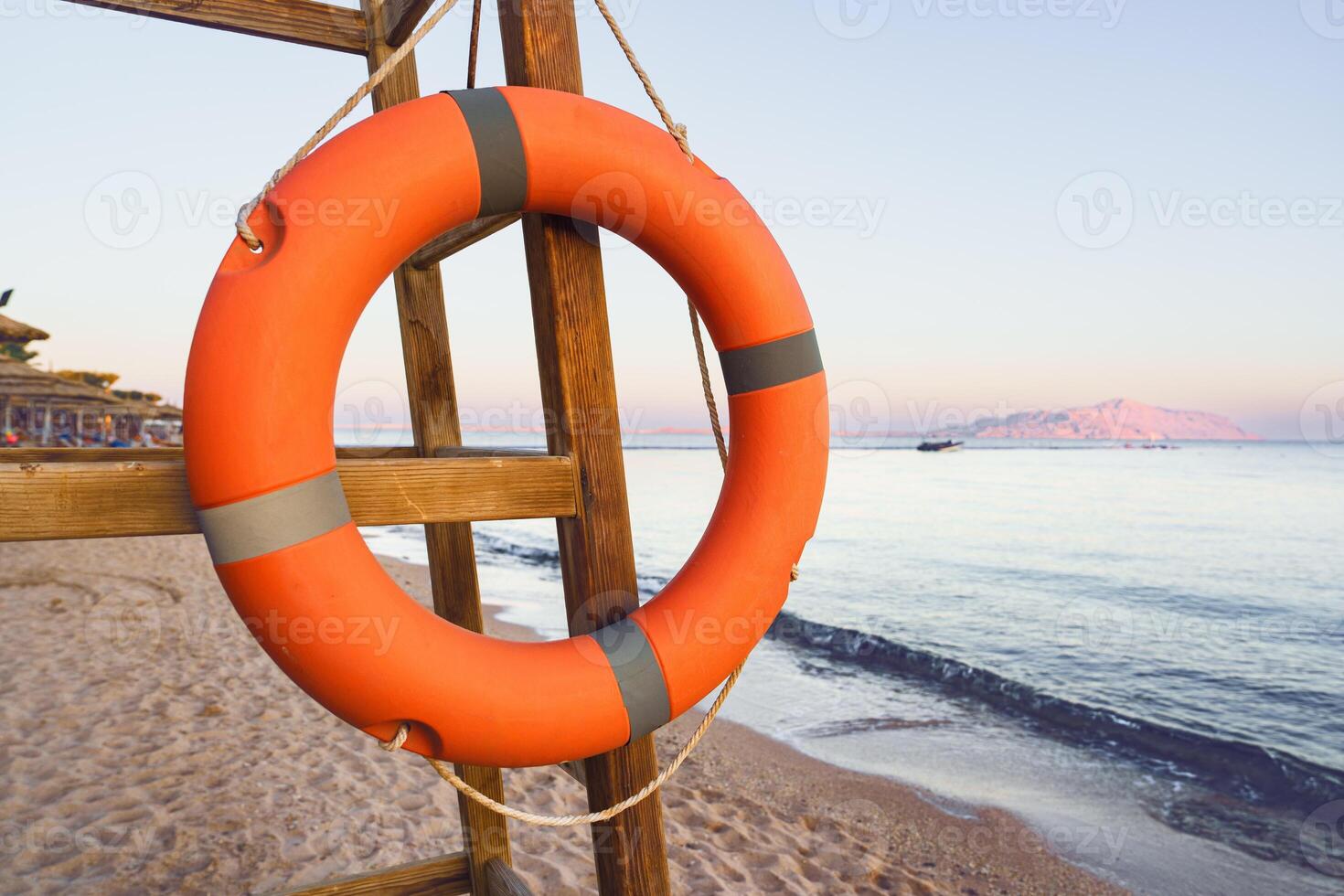 Lifebuoy hangs prominently on wooden stand near tranquil beach at sunset, overlooking calm sea and distant island photo