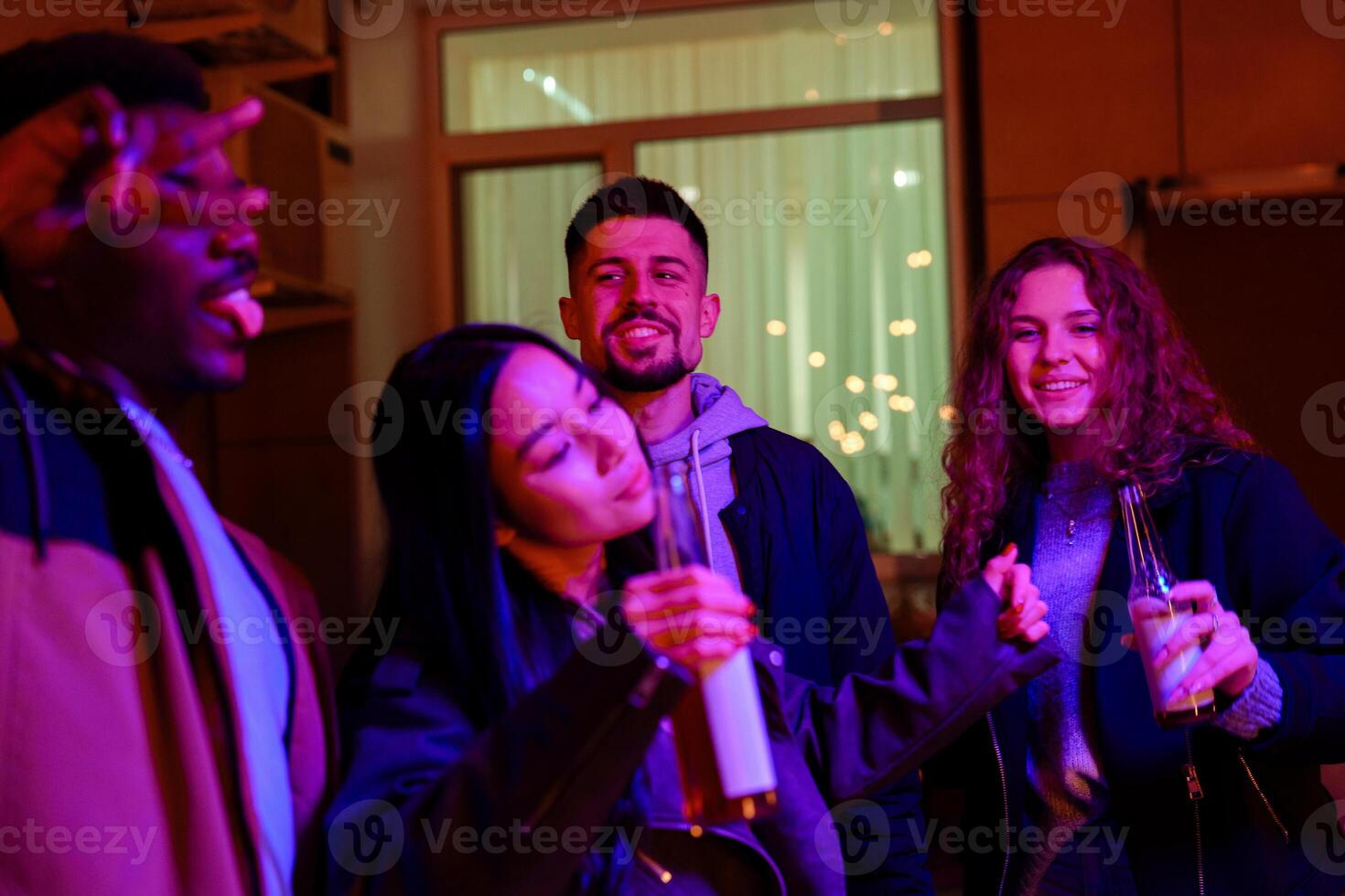 Friends enjoying a lively gathering indoors at night with colorful lights and drinks in hand photo