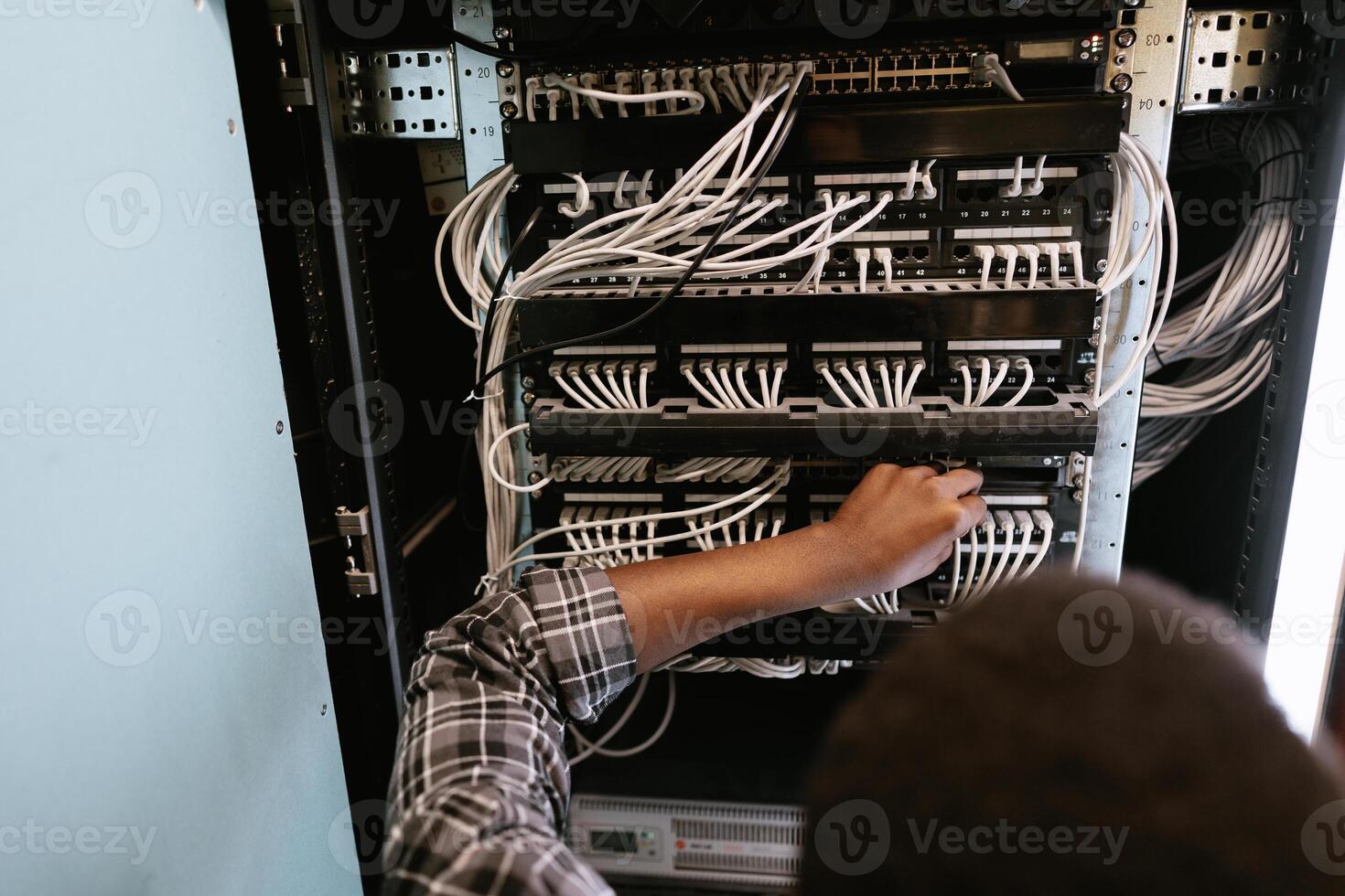 Technician managing network cables in a server room during the afternoon hours photo