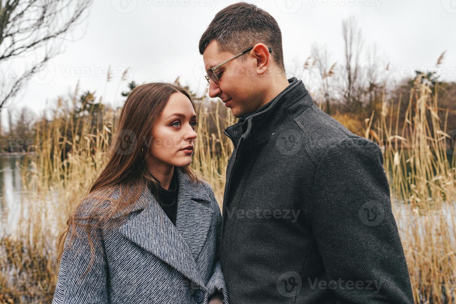 Couple sharing an intimate moment by the lake surrounded by tall grass on a cloudy day photo