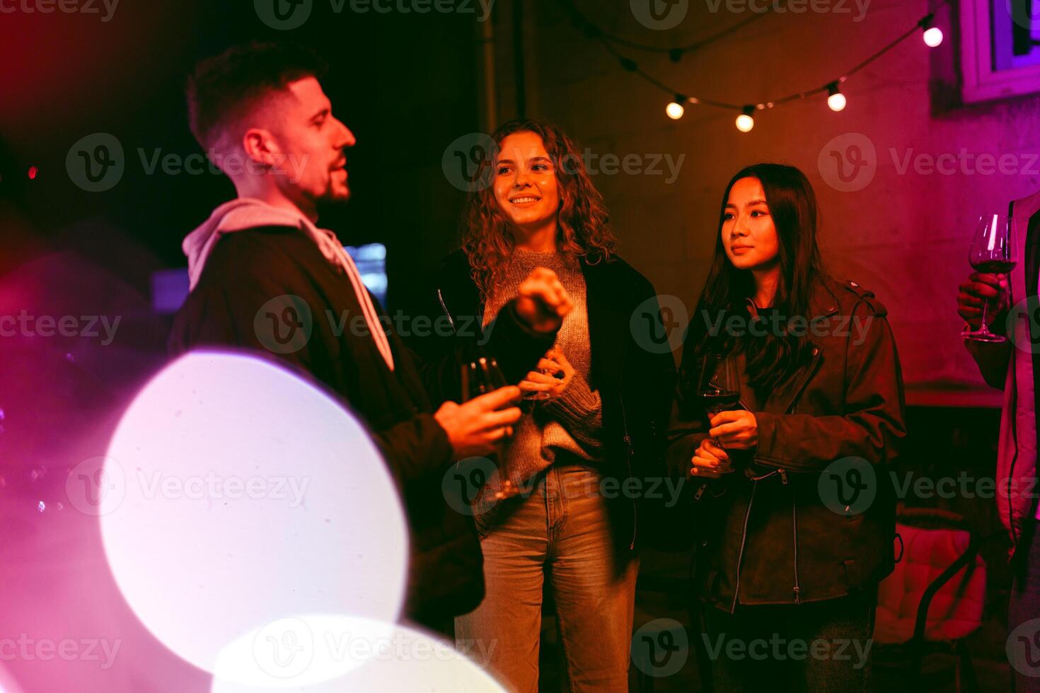 Friends enjoying an evening gathering with drinks and laughter under string lights at an outdoor location photo