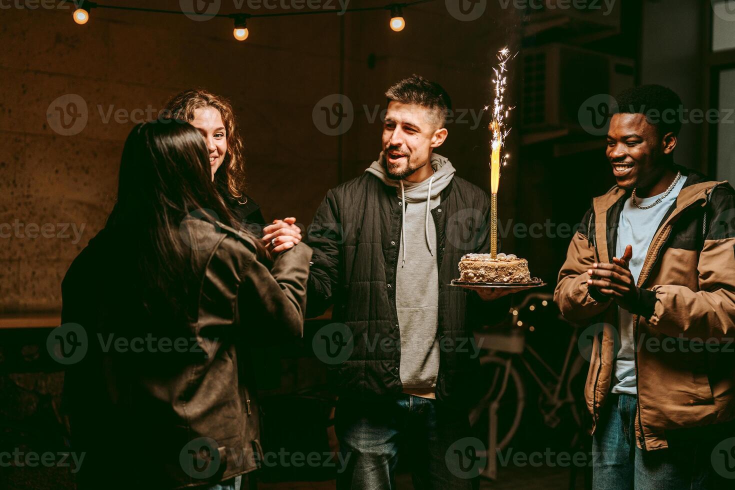 Friends celebrate a birthday with cake and laughter during an evening gathering at a cozy venue photo