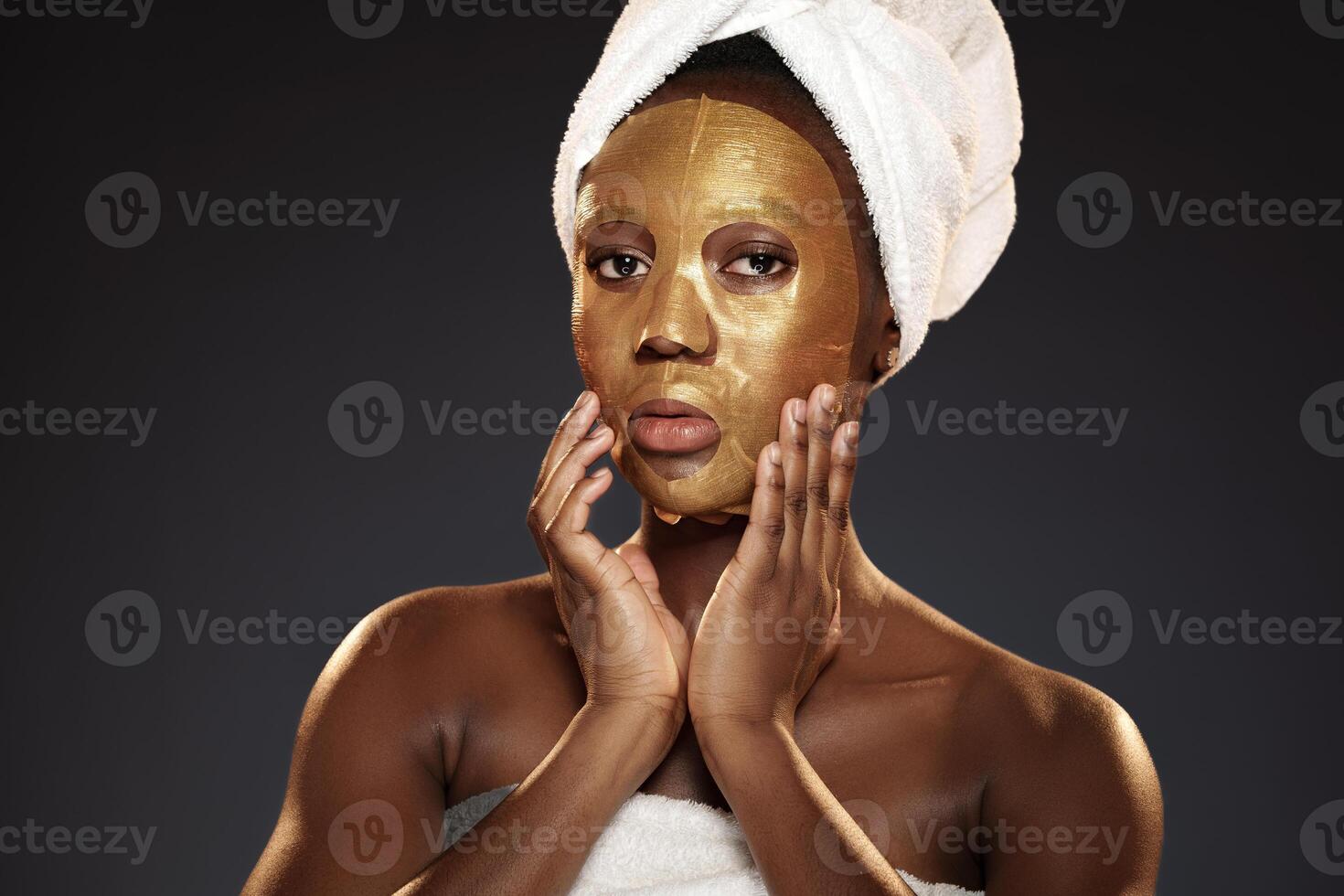 Woman applying gold facial mask while relaxing at a spa with a towel wrapped around her head photo