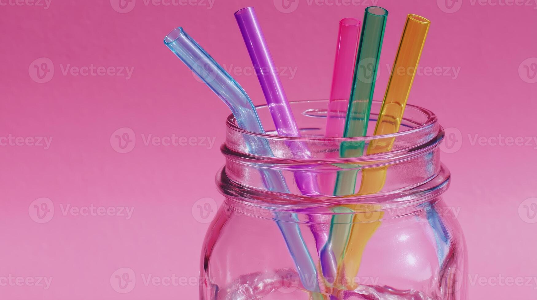 Colorful reusable straws in a glass jar against a vibrant pink background highlight sustainability and eco-friendly choices photo