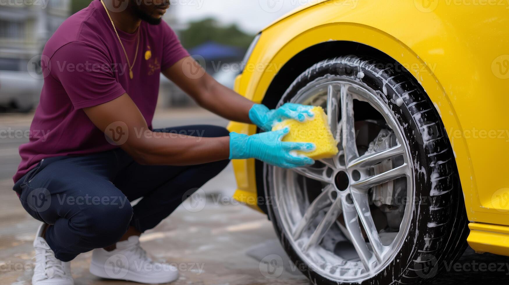 Person cleaning yellow car wheel with sponge during bright day in outdoor car wash area photo