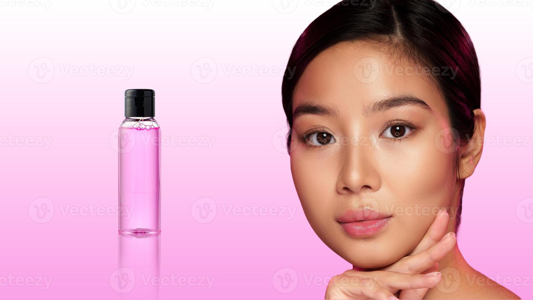 Young woman showcasing skincare product against gradient pink background during a beauty shoot photo