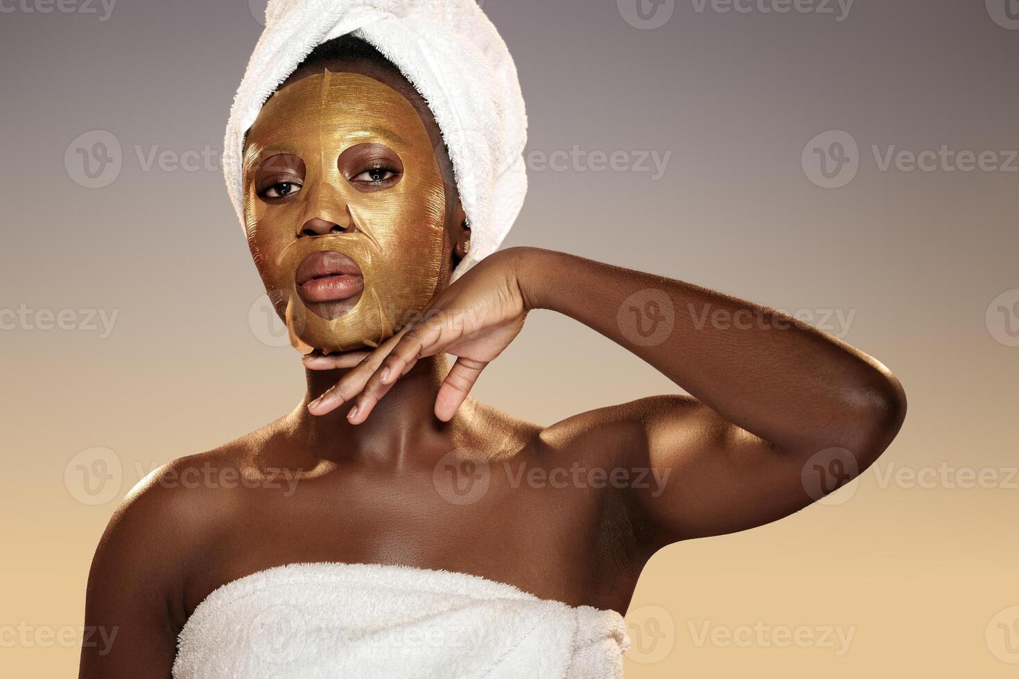 Woman relaxing with a gold face mask while wrapped in a towel in a serene spa-like setting during a beauty routine photo