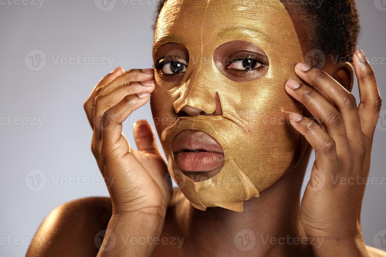 Woman applying a gold facial mask, showcasing skincare routine and self-care on a neutral background photo