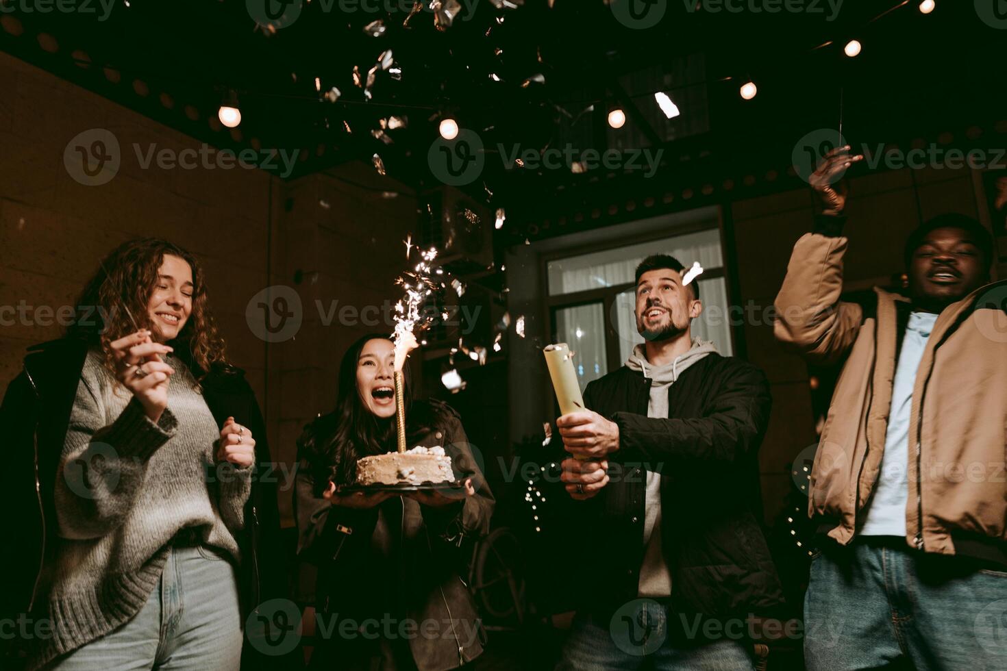 Friends celebrating a birthday with cake, sparkles, and joyful expressions in an indoor party setting photo