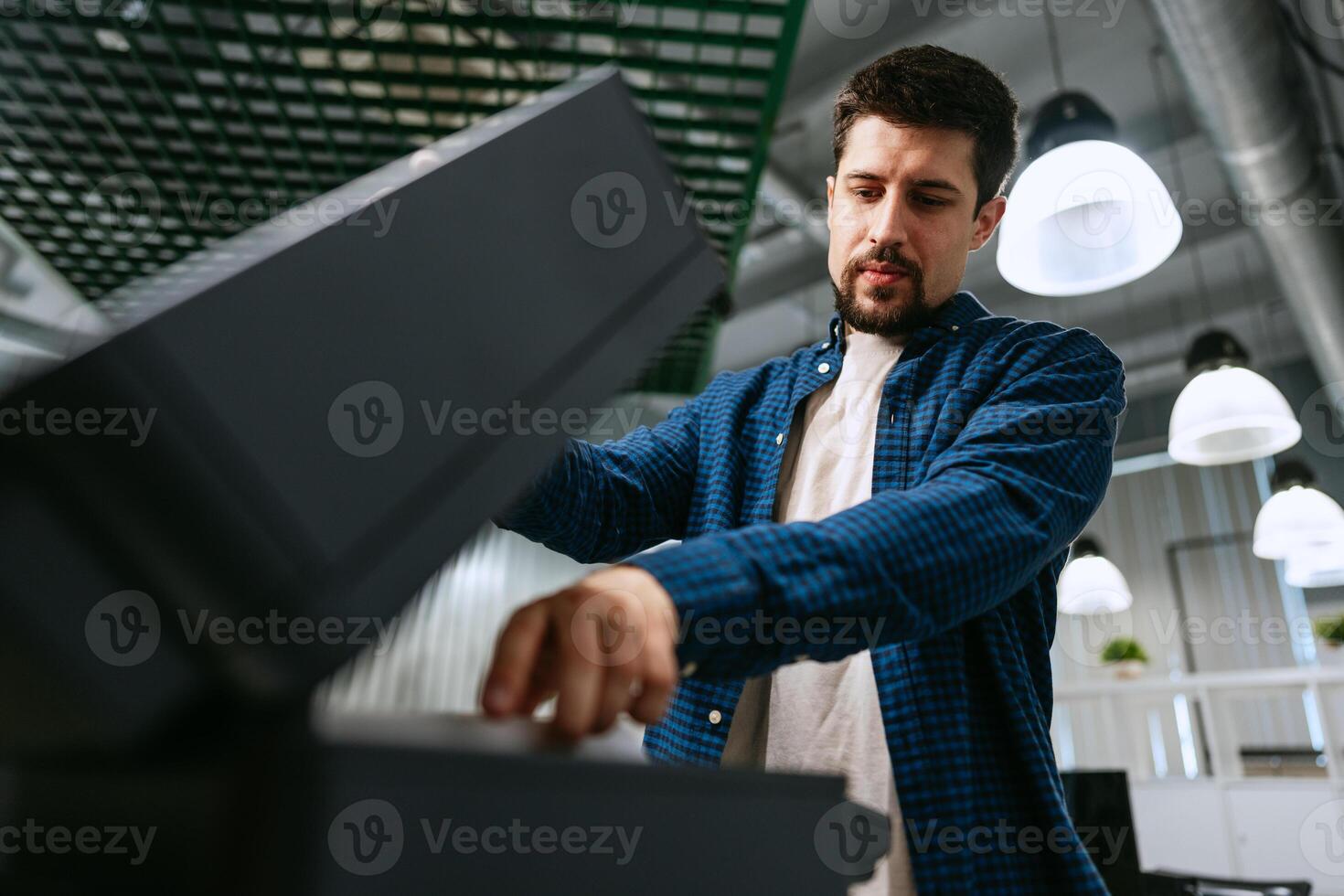 Young man operating a modern office printer while focused on printing documents in a quiet workspace photo