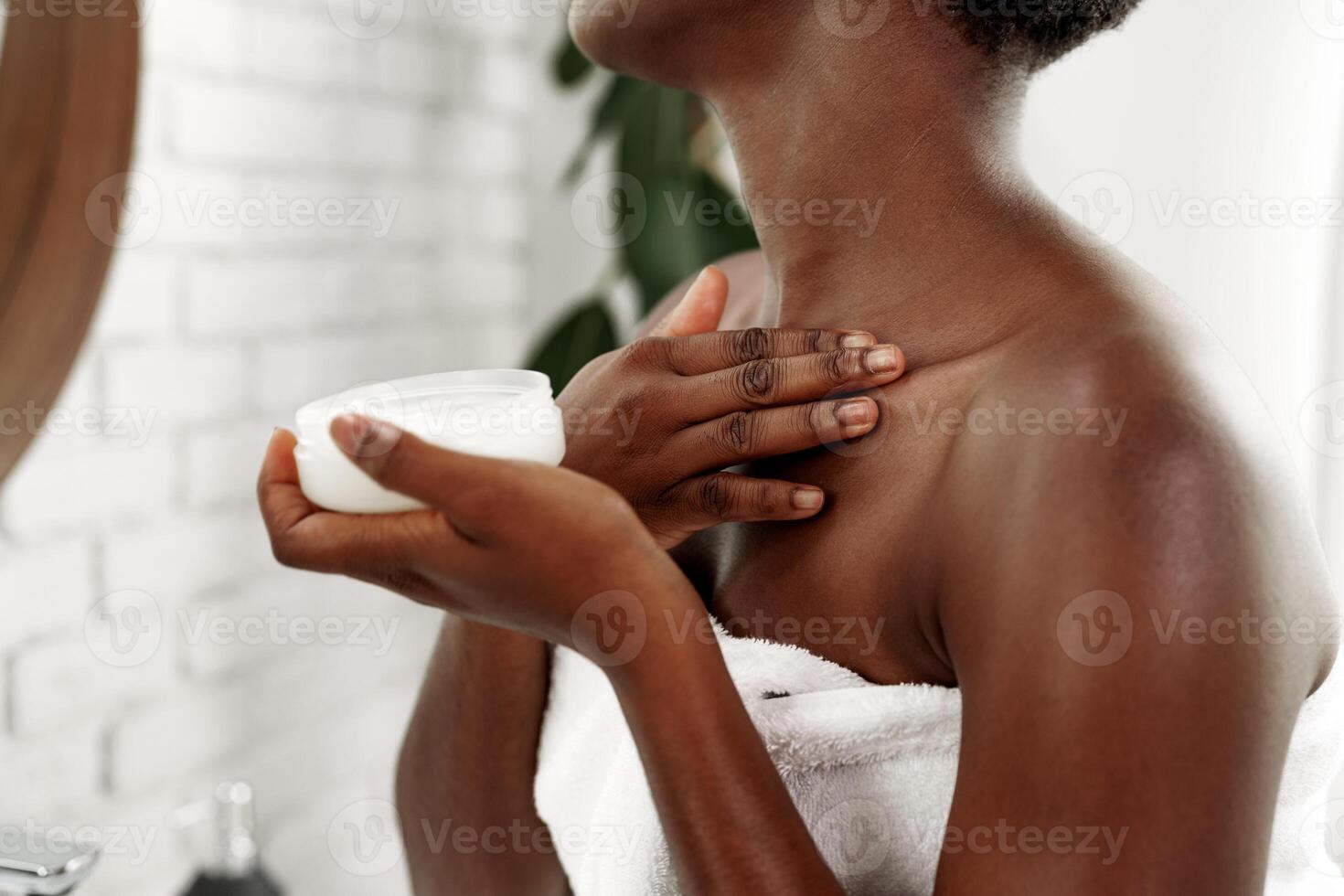 Woman applying moisturizer to her neck in a modern bathroom with light fixtures during a skincare routine photo
