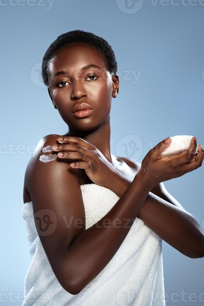Woman applying skin cream during a skincare routine with a soft towel in a calming studio environment photo