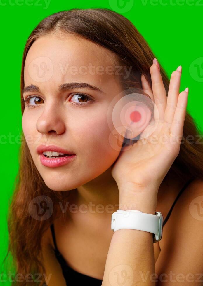 Young woman listening intently with hand to ear against bright green background, showcasing curiosity and engagement in the moment photo
