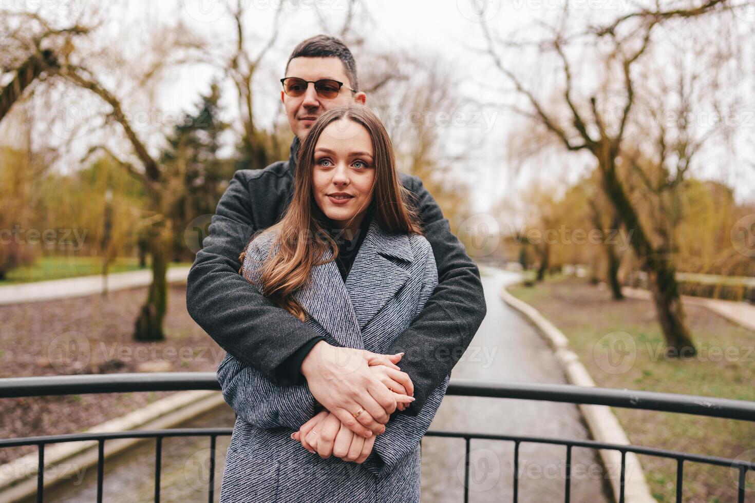 Couple embraces on a scenic bridge during a cloudy day in a tranquil park with trees in early spring photo