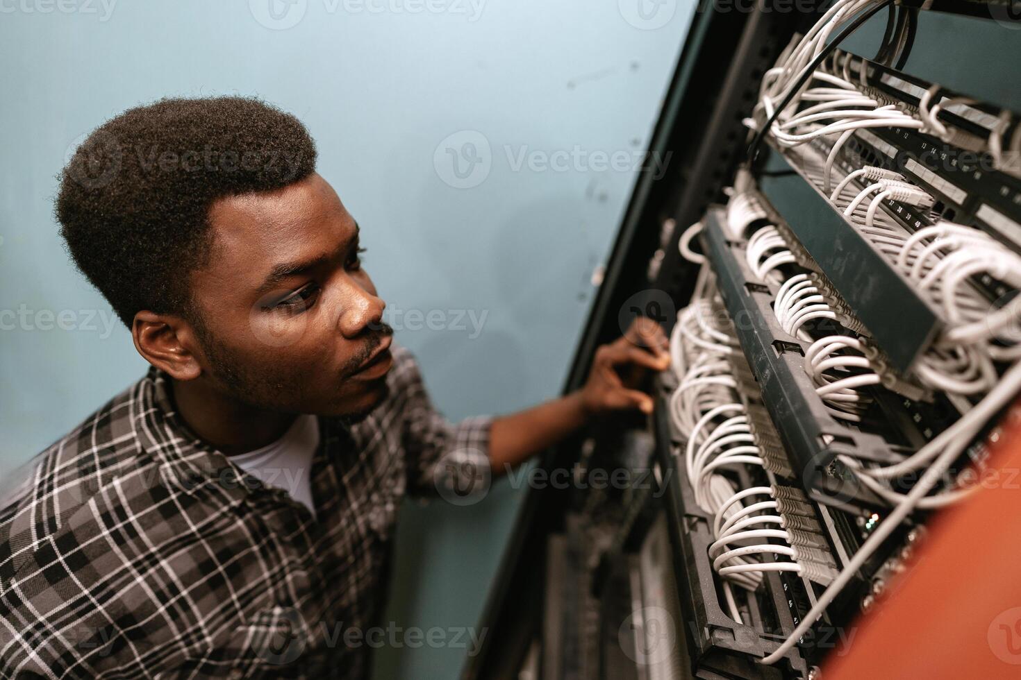 Young technician working on networking cables in a server room during daylight hours photo