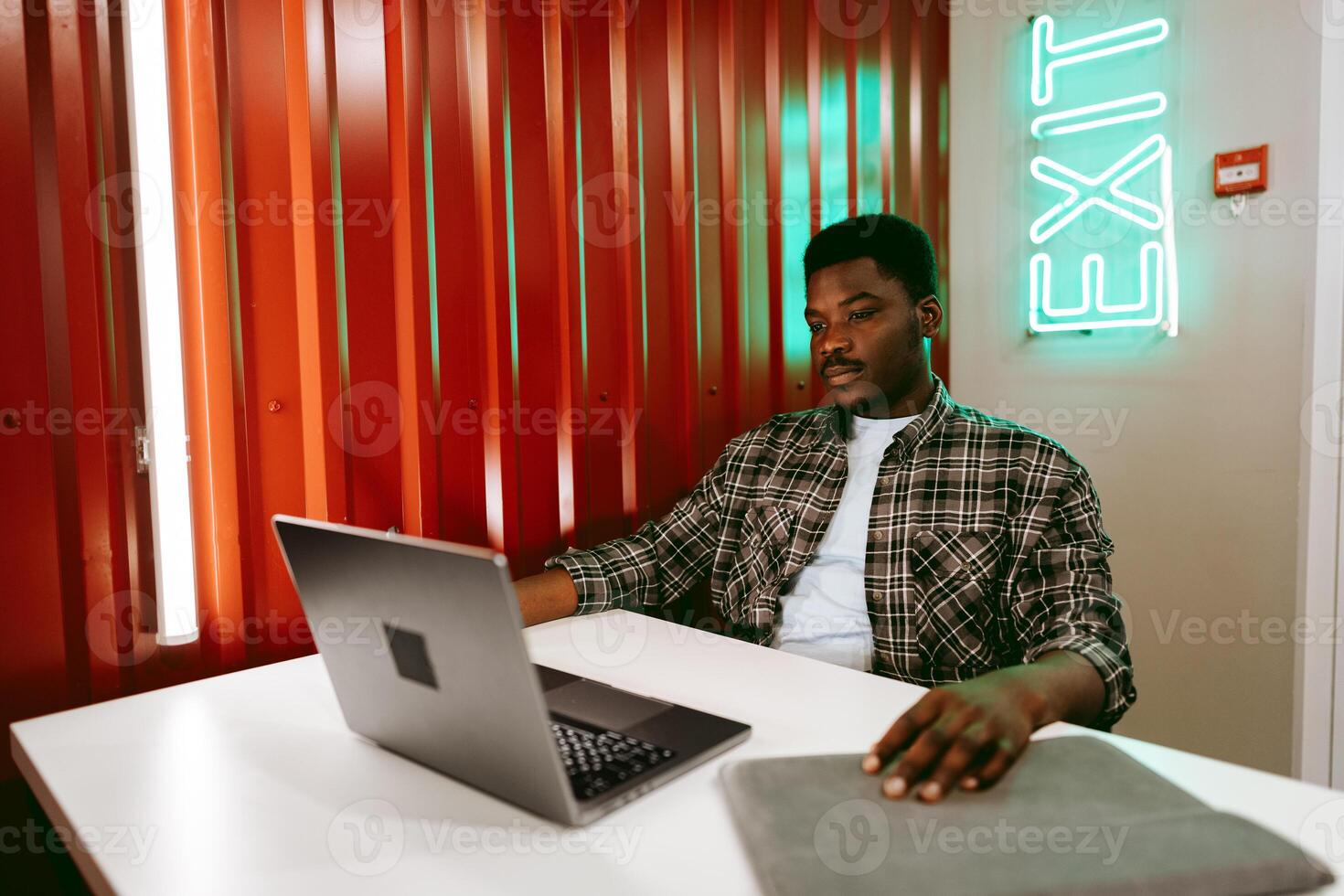 Young man working on a laptop in a modern workspace with vibrant decor and an exit sign photo