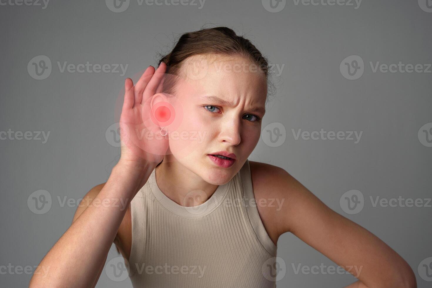Young woman experiencing ear pain and discomfort while holding her hand to her ear in a neutral setting photo
