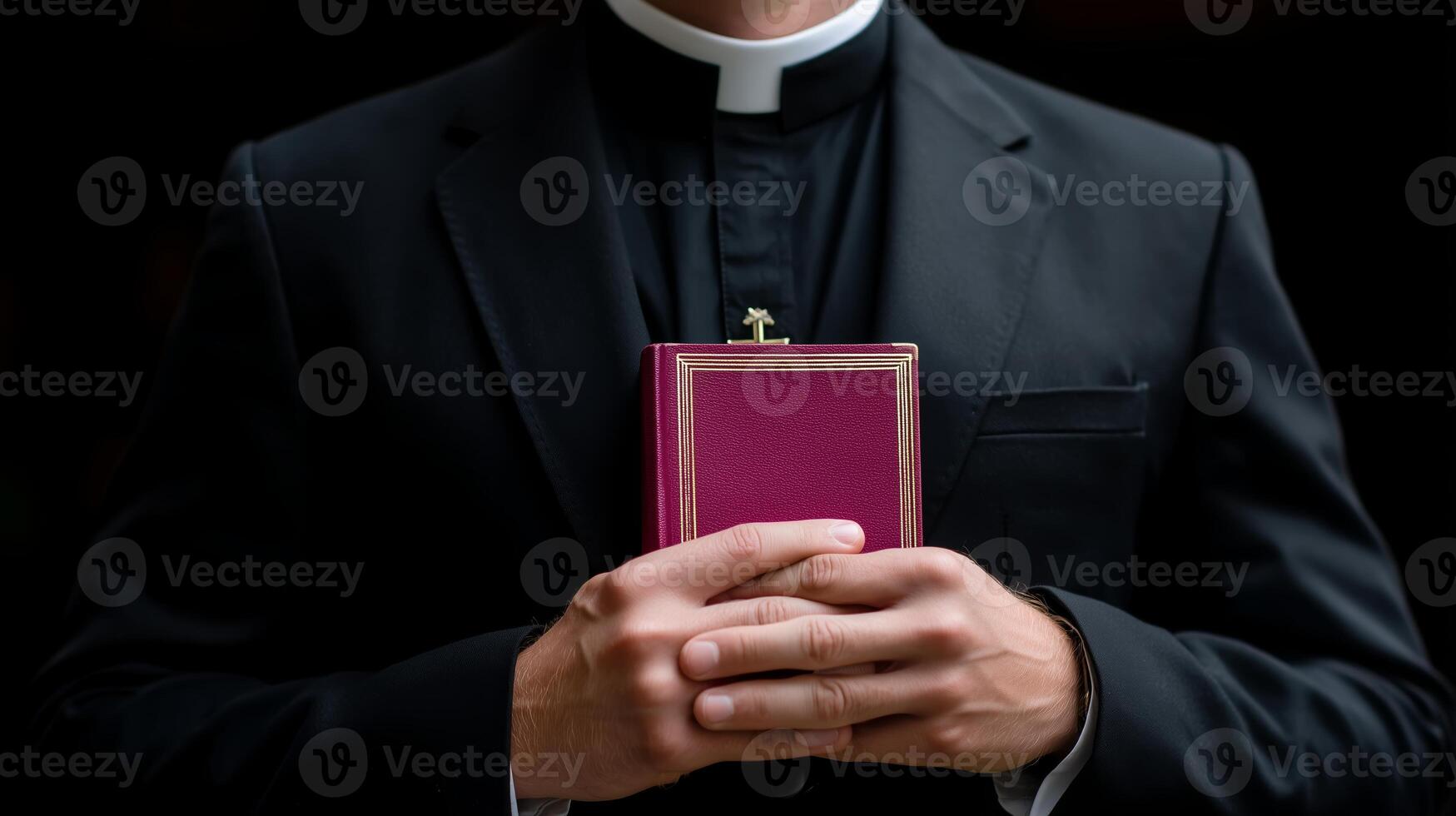 Clergyman holds a prayer book while dressed in formal black attire in a dimly lit setting photo