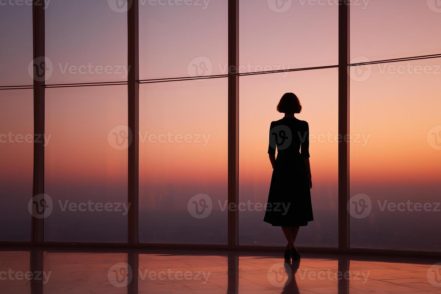 Woman in black dress stands by window at sunset overlooking city skyline photo