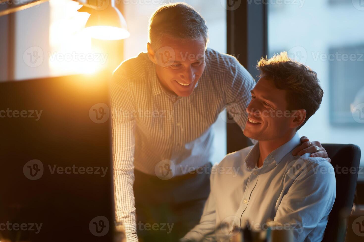 Two colleagues sharing a joyful moment during late evening work at their office with sunlight streaming through the window photo