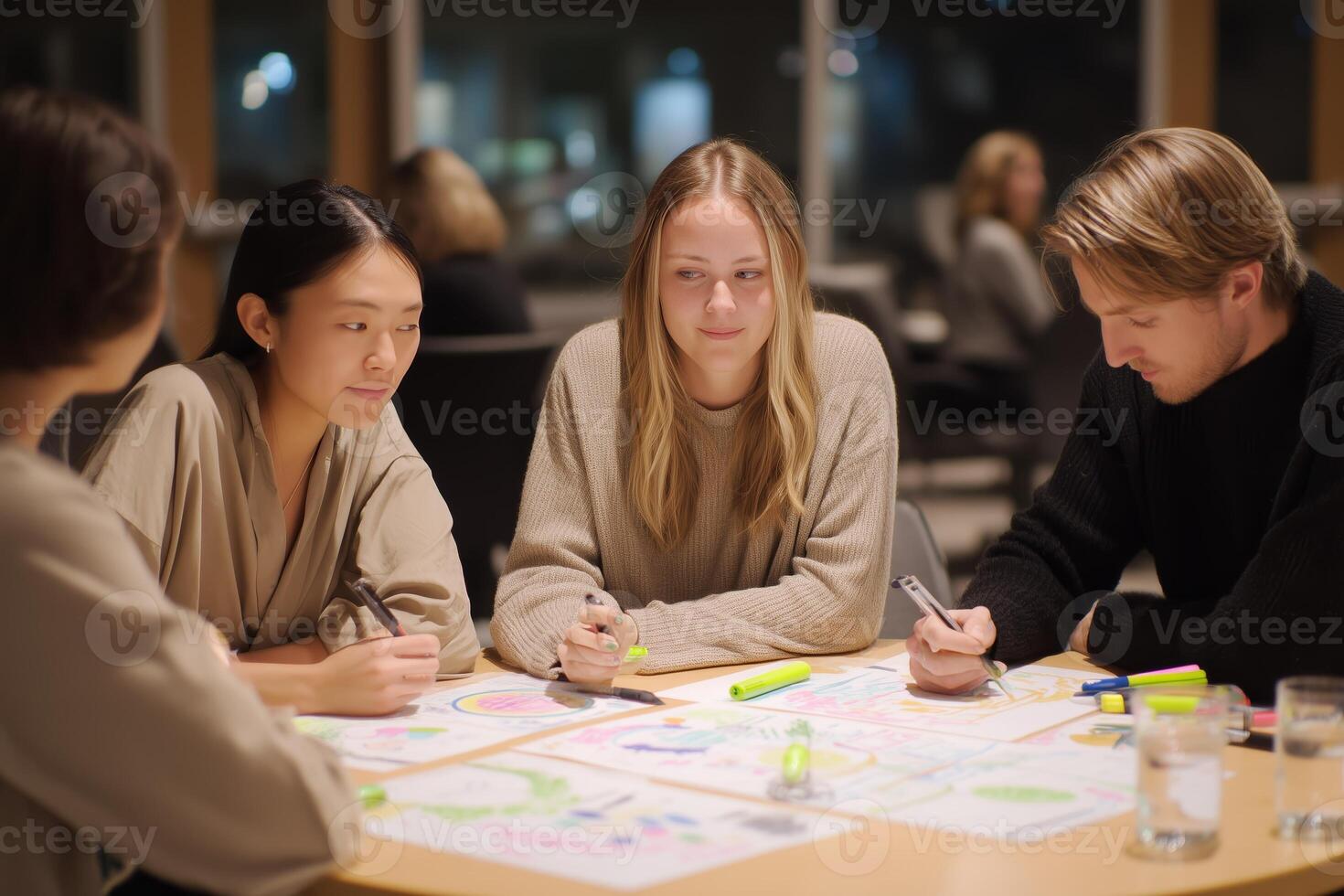 Group of young adults collaborating on creative projects in a modern workspace during the evening hours photo