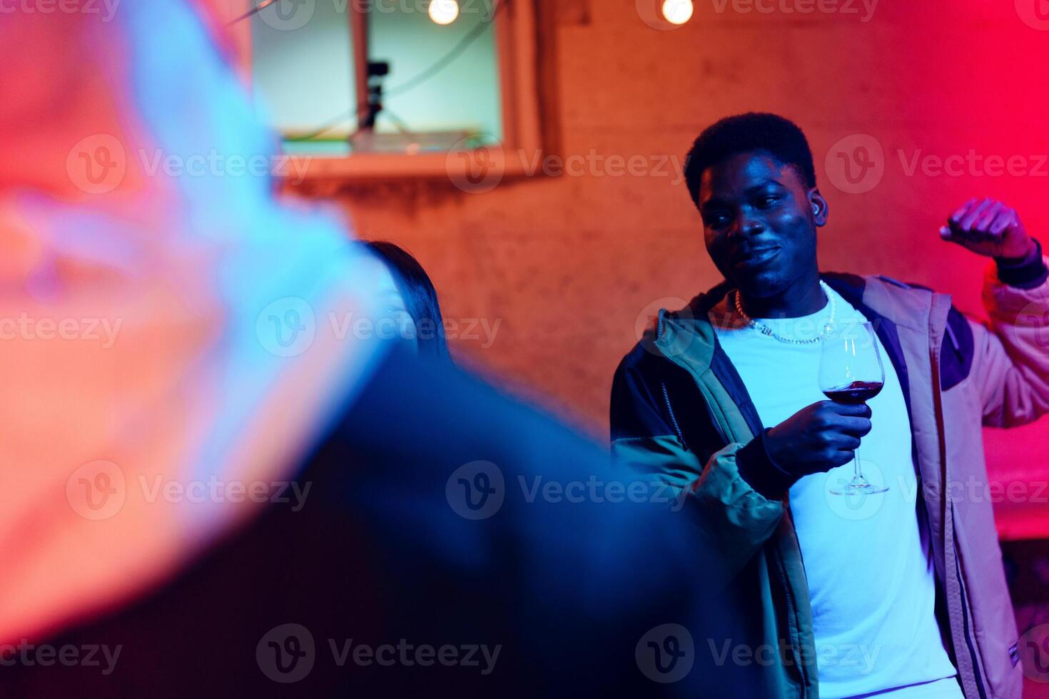 Man enjoying a lively indoor party while holding a glass of red wine in a vibrant atmosphere with colorful lighting photo