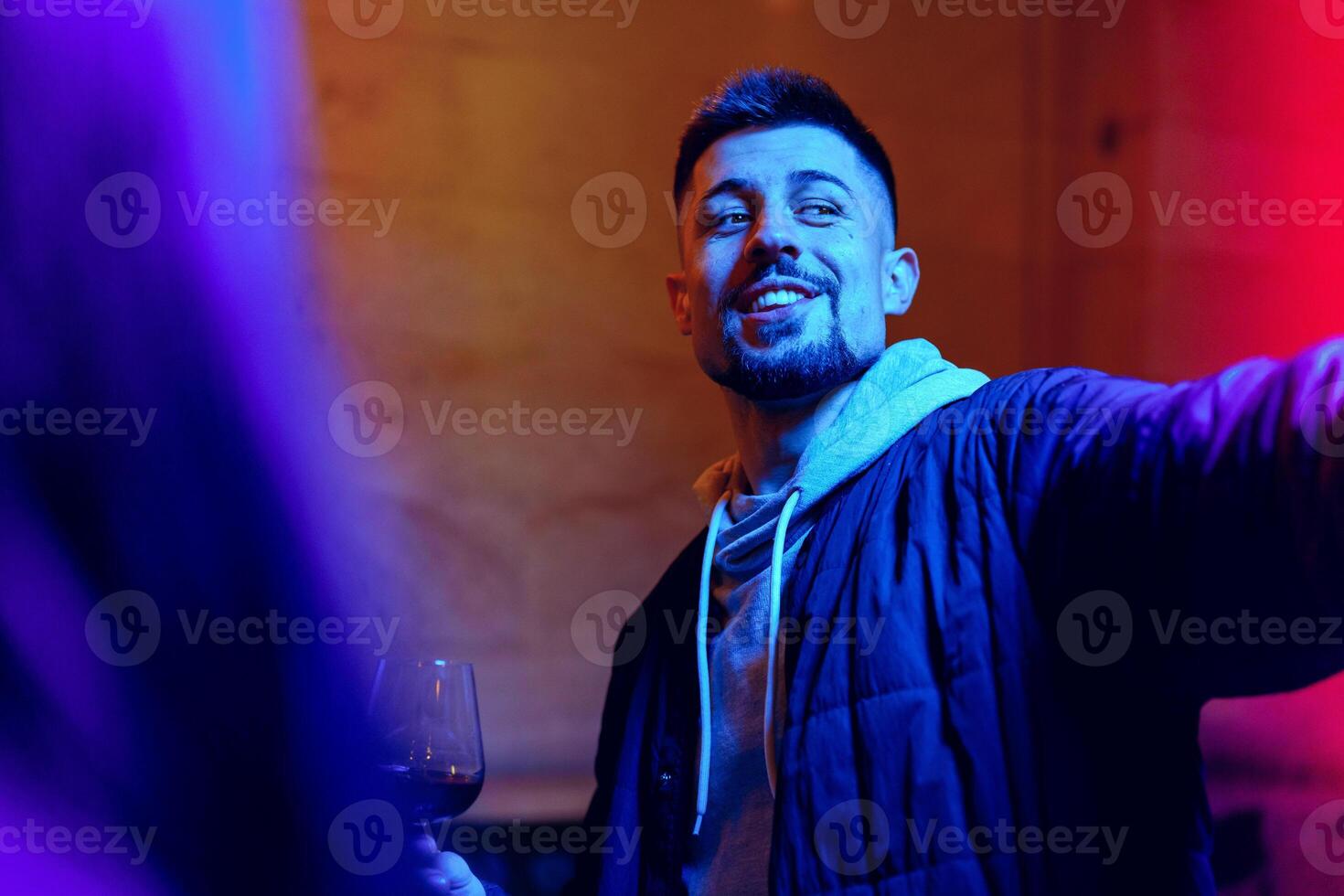 Young man enjoying social gathering while holding a drink with colorful lighting in background photo