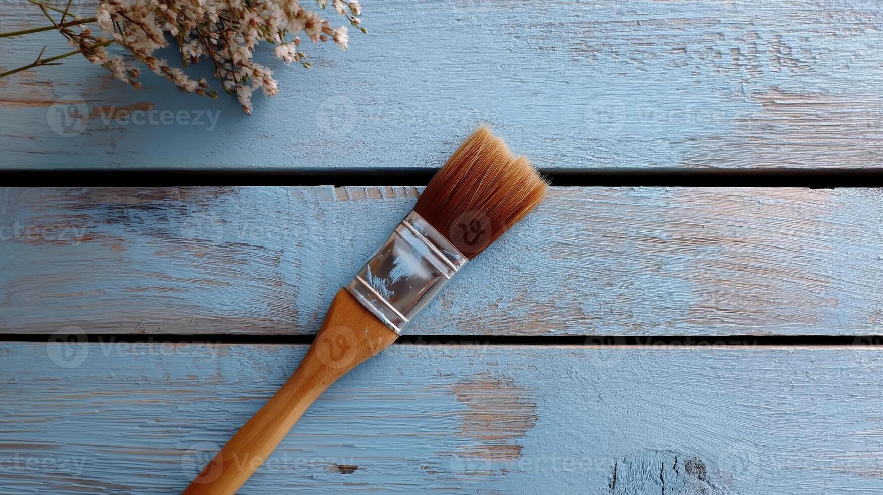 Brush resting on textured blue wooden surface with dried flowers in background during daylight photo