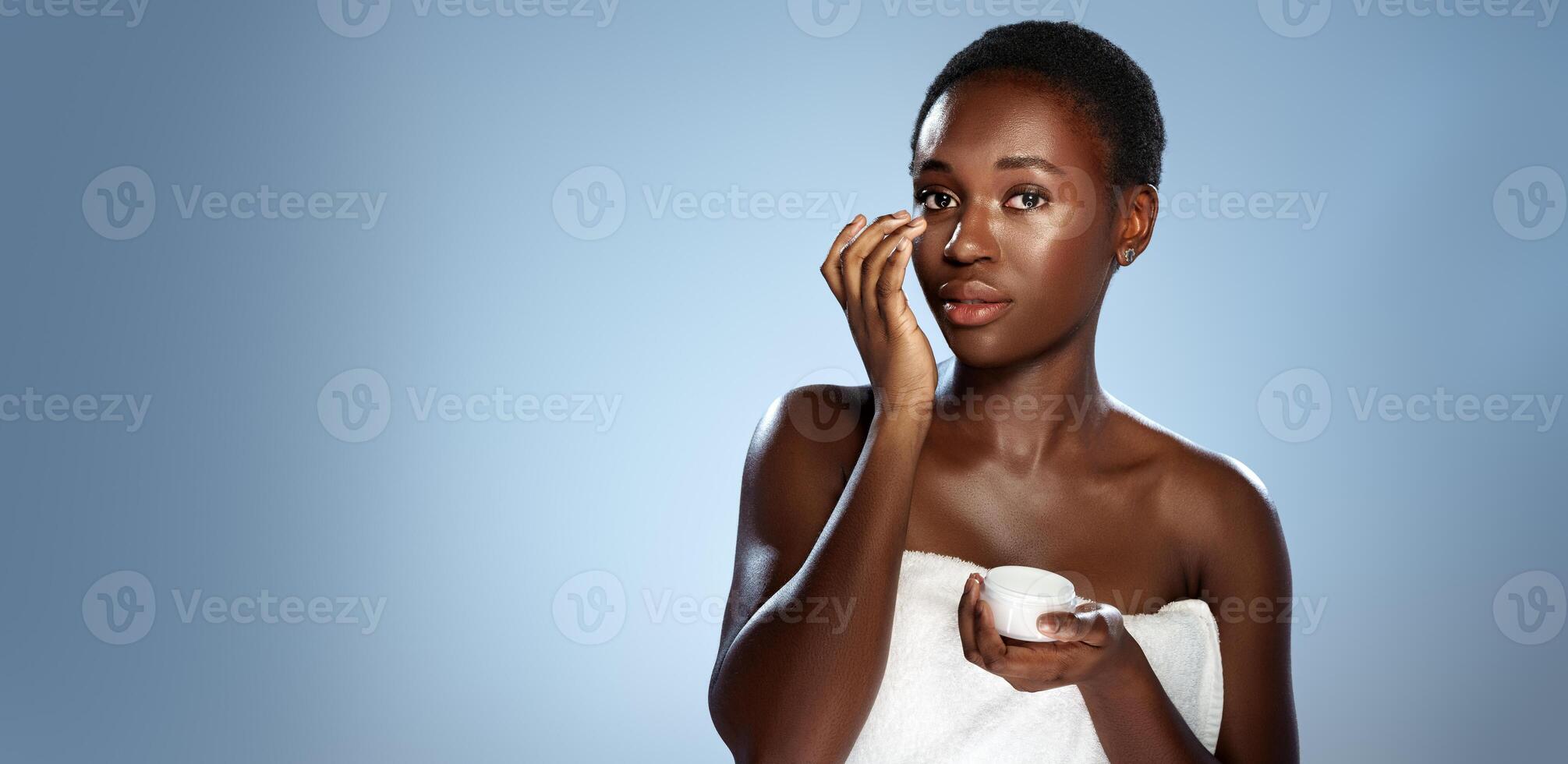 Woman applying skincare product in minimalistic studio setting during daytime routine photo